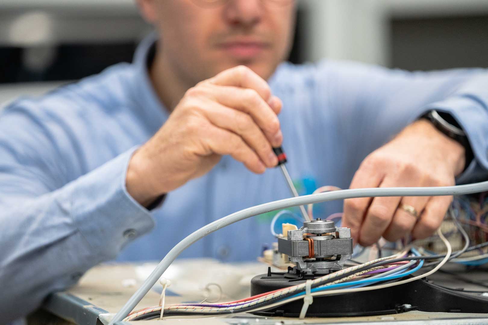 Elektrohersteller Jan, de collega van Marc Leyre, sleutelt aan de elektrische bedrading van een microgolfoven in de werkplaats.