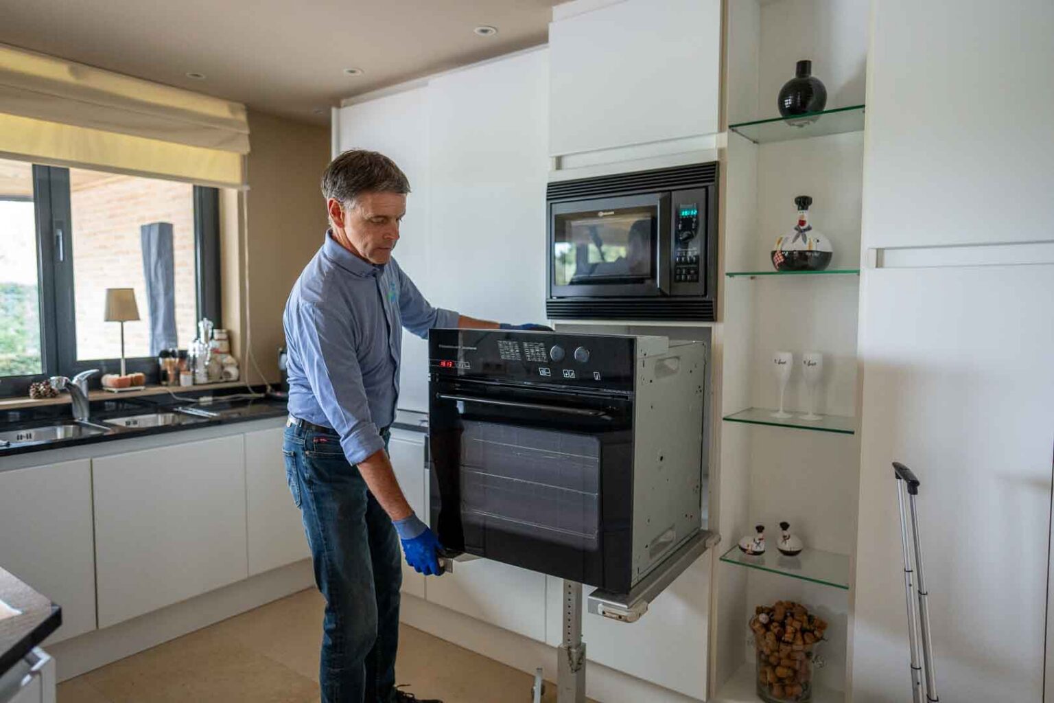 Dokter Elektro haalt een ingebouwde oven uit het keukenmeubel voor herstelling. Marc Leyre aan het werk in de keuken van een particulier.
